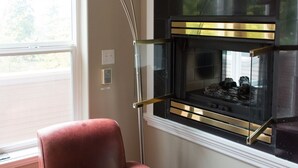 A room with a leather armchair, a modern floor lamp, and a fireplace with a glass enclosure. - Everyone Welcome, Cozy retreat walking distance to  Butchart Gardens. (Brentwood Bay)