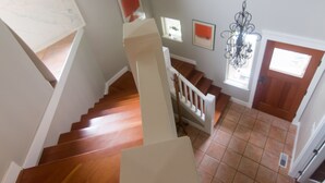 A staircase with wooden steps and white railings, leading to a room with a tiled floor and a door with a window. - Everyone Welcome, Cozy retreat walking distance to  Butchart Gardens. (Brentwood Bay)