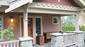 A covered porch with a stone bench, a wooden door, and a small table with a radio. - Everyone Welcome, Cozy retreat walking distance to  Butchart Gardens. (Brentwood Bay)