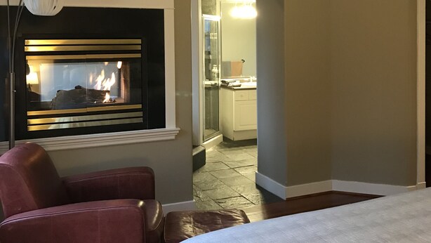 A hotel room with a fireplace, a ceiling fan, a TV mounted on the wall, and a bed. - Everyone Welcome, Cozy retreat walking distance to  Butchart Gardens. (Brentwood Bay)