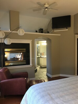 A hotel room with a fireplace, a ceiling fan, a TV mounted on the wall, and a bed. - Everyone Welcome, Cozy retreat walking distance to  Butchart Gardens. (Brentwood Bay)