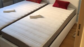 Een kamer met twee eenpersoonsbedden, elk met een witte matras en rode kussens.