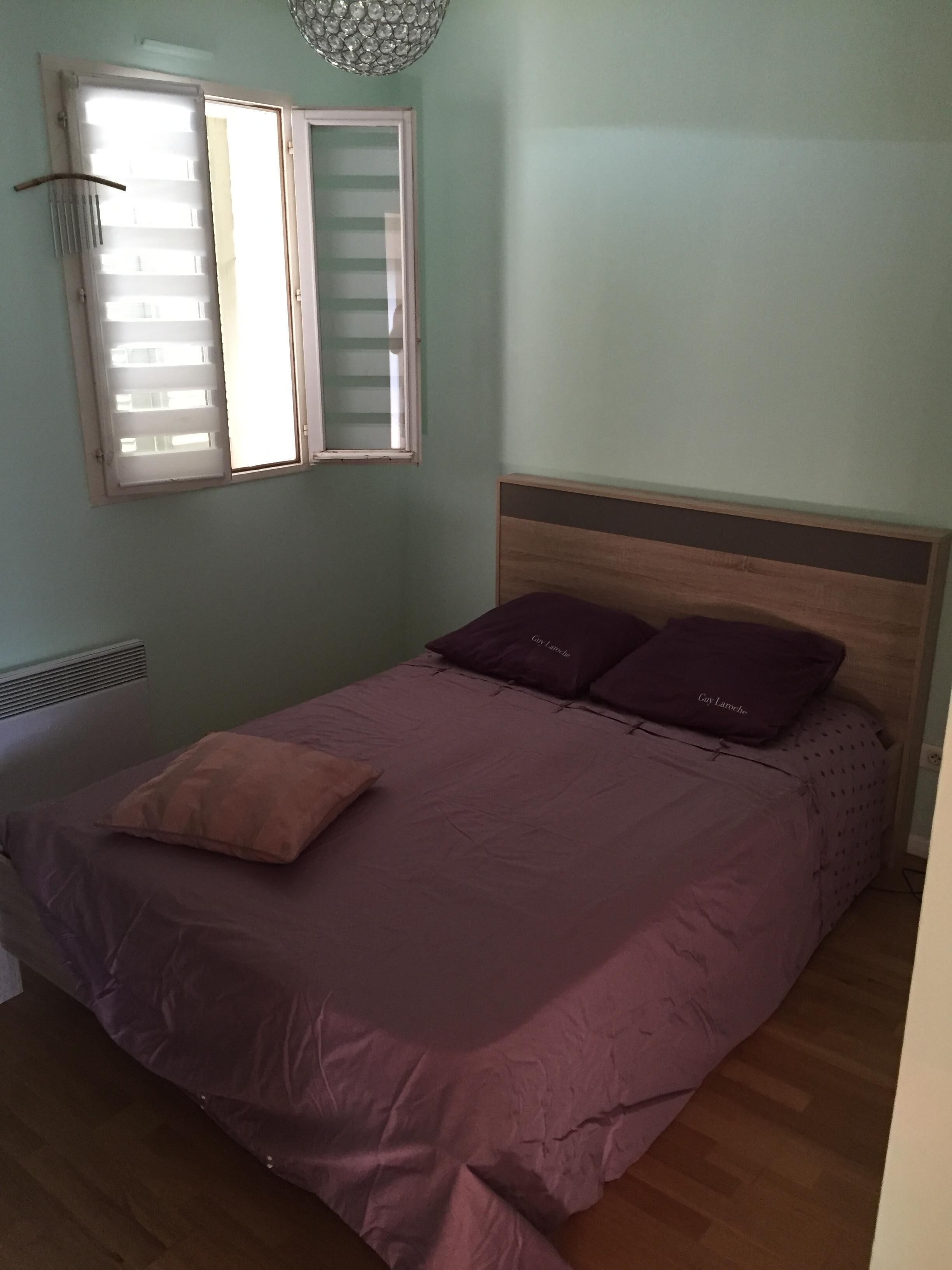Ein Schlafzimmer mit einem Bett, zwei Kissen, einem Fenster mit Jalousien und einer Heizung.