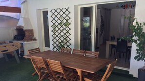 Een houten eettafel met zes stoelen, een tafelvoetbaltafel en een bakoven in een patio met kunstgras.