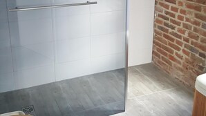 A room with a glass shower door, a wooden stool, and a brick wall.