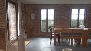 A room with brick walls, large windows, a wooden table, and chairs. There are two metal containers on the floor.