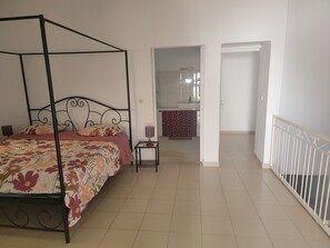 A bedroom with a four-poster bed, a bedside table, and a bathroom visible through an open door. - DOLMEN DE M'BOUR - Your next dream vacation, 5 min from the ocean (M'bour)