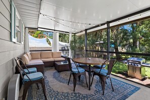 Un patio techado con sofá, sillas, una mesa y una parrilla.