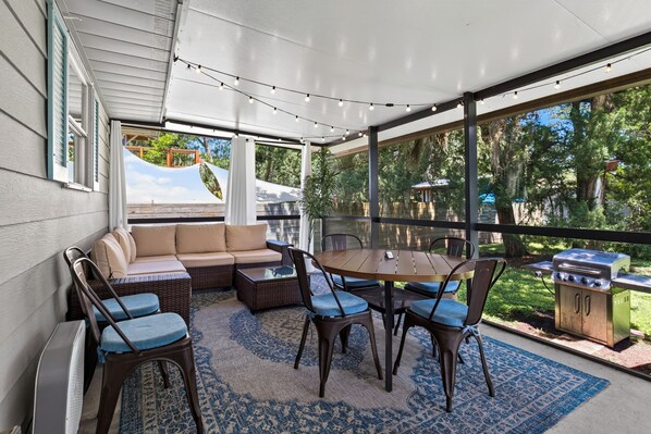 A covered patio with a sofa, chairs, a table, and a grill.