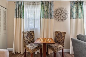 Una habitación con un tablero de ajedrez sobre una mesa, dos sillas estampadas y un adorno en la pared.