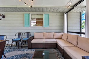Une véranda avec un canapé, des fauteuils et une table en osier.