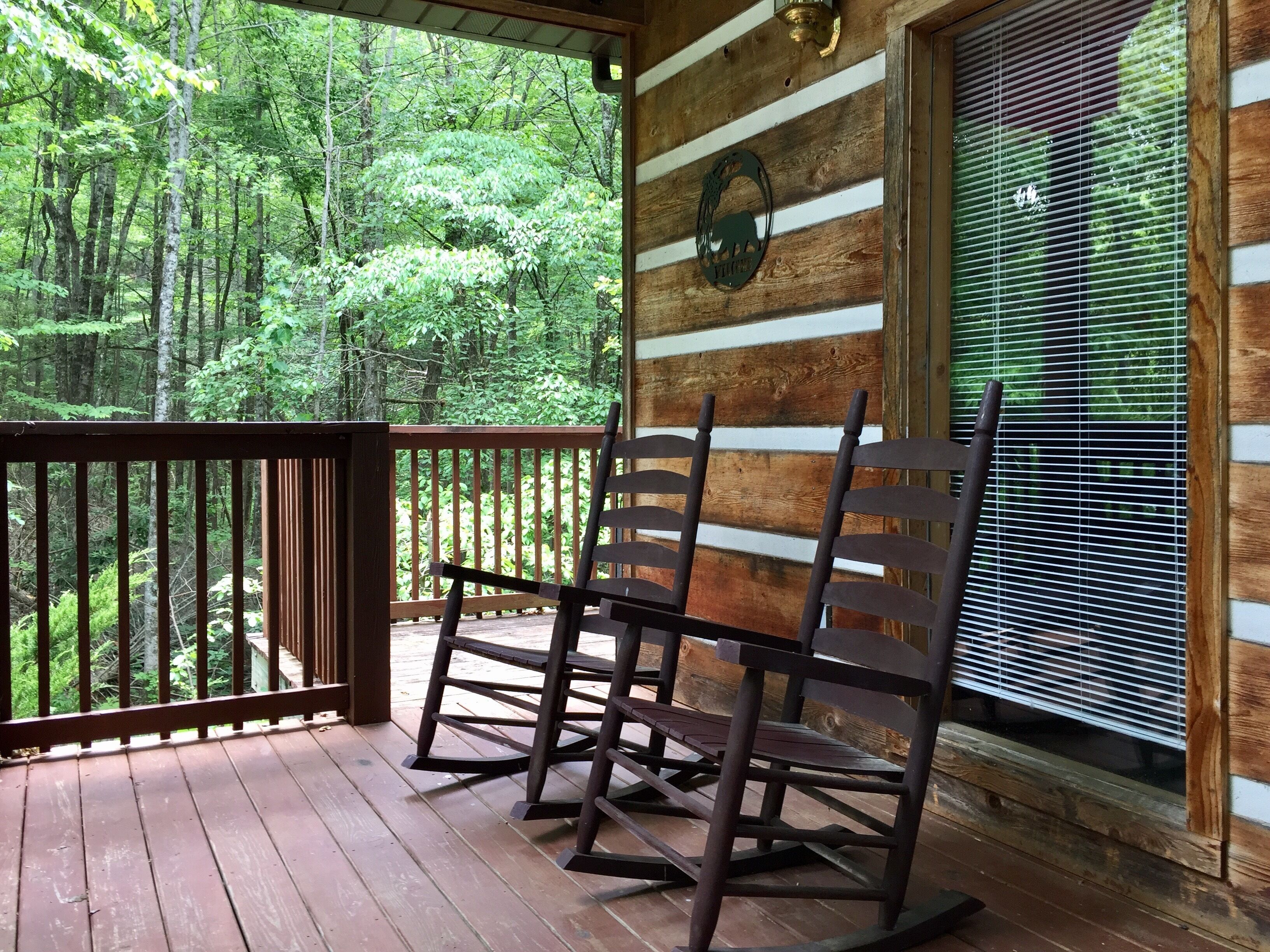A wooden deck with rocking chairs, a wooden wall with horizontal planks, and a window with blinds.