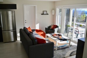 Een moderne woonkamer met een bank, fauteuil en salontafel. Er is een schuifdeur die leidt naar een buitenruimte met uitzicht op de oceaan.