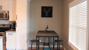Una cocina con armarios blancos, microondas, cafetera y una mesa con dos taburetes.