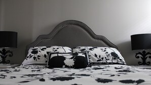 Una cama con cabecera oscura, dos lámparas negras a cada lado y una colcha de estampado floral.