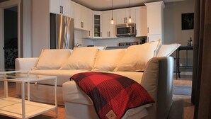 Una sala moderna con un sofá blanco, una mesa de centro de vidrio y una manta roja a cuadros.