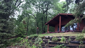 Une cabane en bois dotée d’un porche couvert, entourée d’un jardin où poussent différentes plantes et où l’on trouve des rochers.