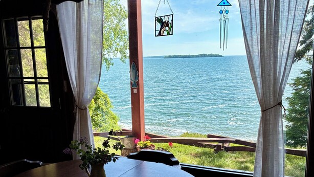 Une pièce avec une table, des chaises, une fenêtre avec des rideaux, un objet décoratif suspendu et une vue sur l’eau.