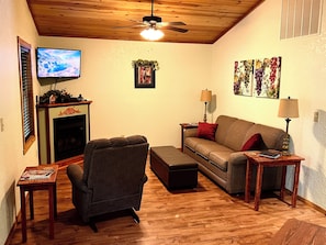 Una sala acogedora con chimenea, televisión, sofá, sillón y techo de madera.