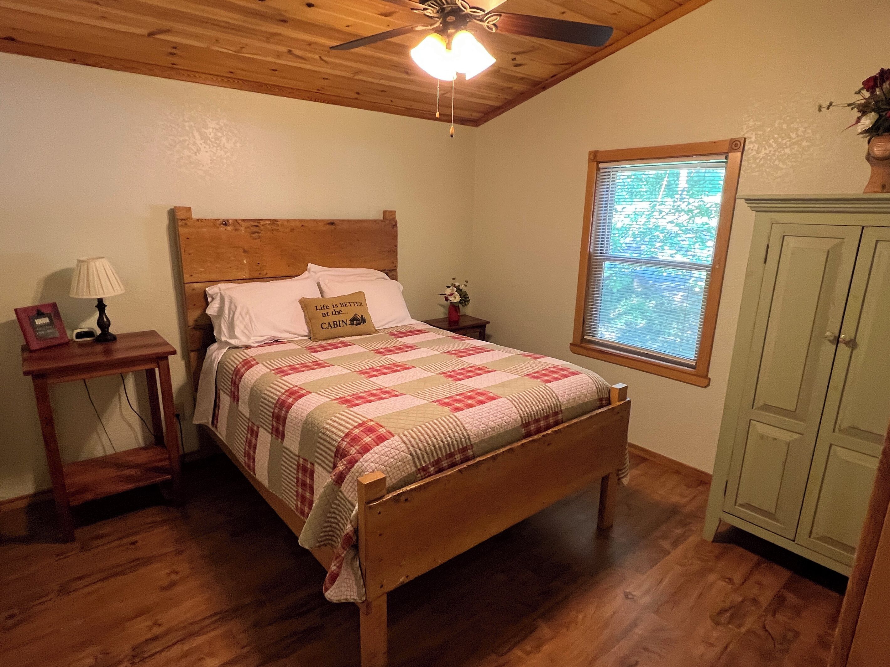 Une chambre avec un lit en bois, une table de chevet avec une lampe, une fenêtre donnant sur un beau paysage et une armoire verte.