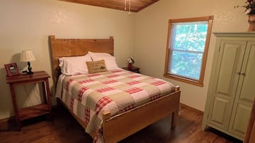 Une chambre avec un lit en bois, une table de chevet avec une lampe, une fenêtre donnant sur un beau paysage et une armoire verte.