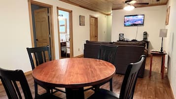 Un coin repas comprenant une table ronde en bois et des chaises, un canapé, un téléviseur et une lampe.