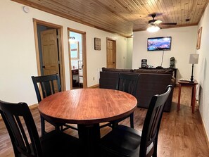 A dining area with a round wooden table and chairs, a sofa, a television, and a lamp. - Exceptional Cabin on Shawnee Wine Trail near Alto Pass and Bald Knob Cross (Alto Pass)