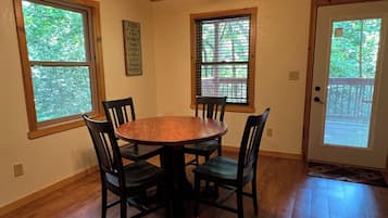 A dining area with a wooden table and chairs, large windows with blinds, and a ceiling fan.
