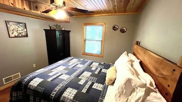 A bedroom with a wooden ceiling, a bed with a quilt, a window with blinds, and a ceiling fan.
