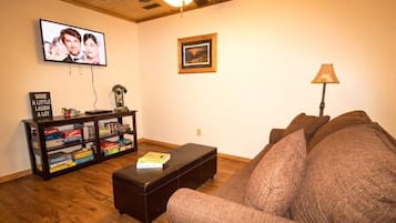 Un salon comprenant un canapé, une table basse, une bibliothèque, un téléviseur et un ventilateur de plafond.