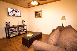A living room with a sofa, a coffee table, a bookshelf, a television, and a ceiling fan.