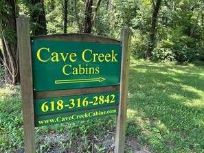 Señal direccional para Cave Creek Cabins con una flecha apuntando a la derecha, número de contacto y dirección web.