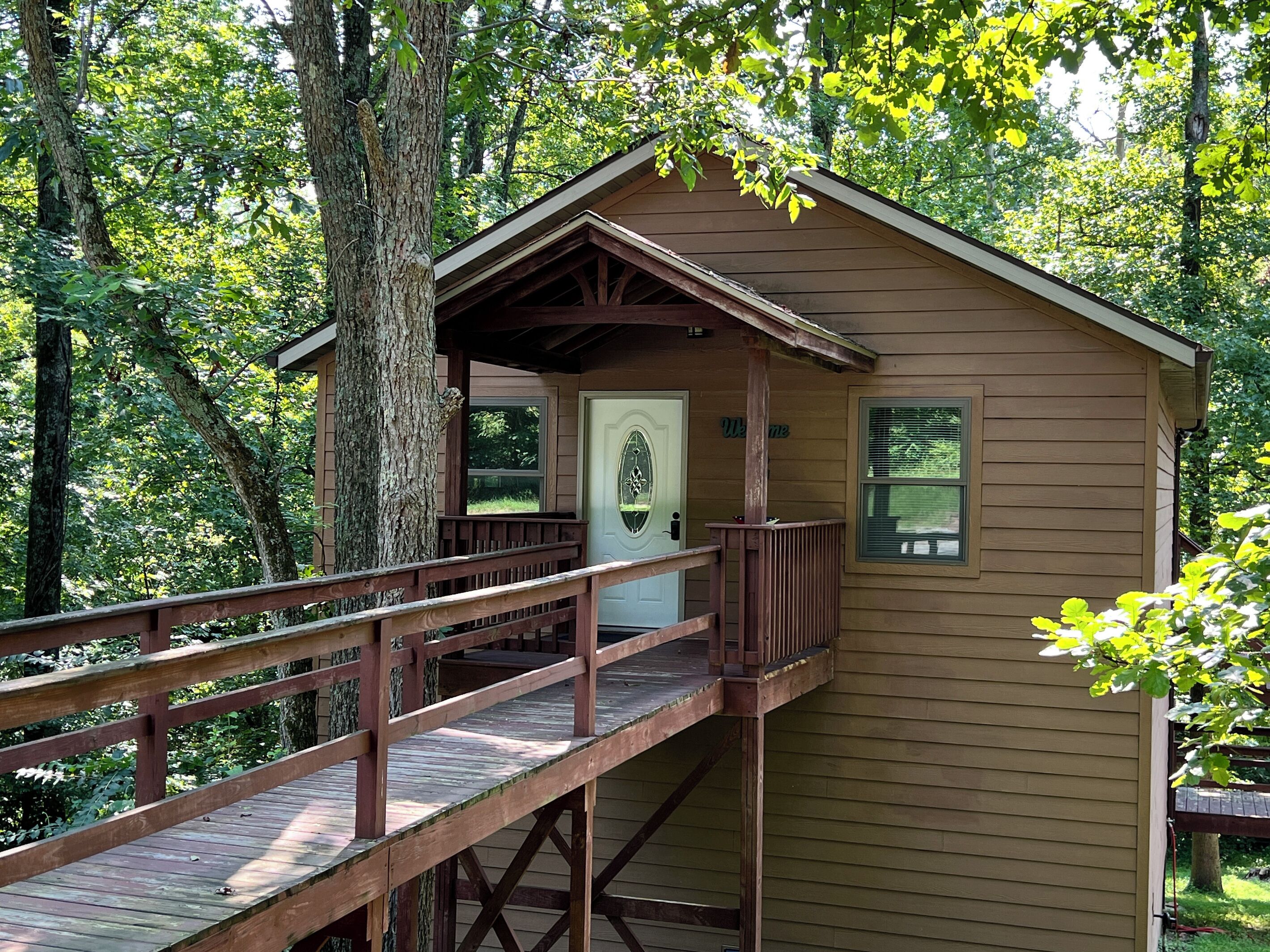 A wooden cabin with a porch and a deck, surrounded by trees.