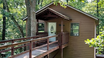 A wooden cabin with a porch and a deck, surrounded by trees.