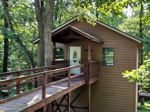 A wooden cabin with a porch and a deck, surrounded by trees.