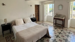 Ein Schlafzimmer mit einem großen Bett, einem Nachttisch, einem kleinen Tisch und einem Fenster mit Blick auf Grünflächen.