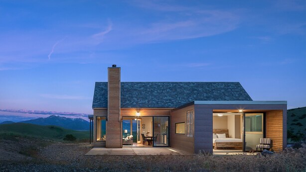 A modern house with a large glass door entrance, a fireplace, and a view of the mountains.