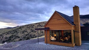 A wooden cabin with a large glass window, a chimney, and a gravel driveway.
