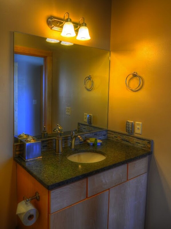 Un baño con lavamanos de encimera de granito, un espejo y dos lámparas fijadas a la pared.