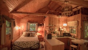 A cozy cabin interior with a wooden bed, a small kitchenette, and a dining area.