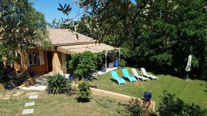Uma casa com área de pátio, um pequeno jardim e um gramado com espreguiçadeiras.