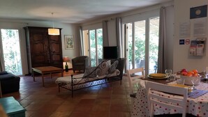 Uma sala de estar ampla com sofá, mesa de jantar posta com pratos e copos, e vista através de grandes janelas.