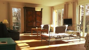 Um quarto iluminado pelo sol com um sofá, uma poltrona, uma mesa e uma televisão.