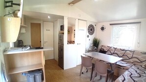 Een knus woongedeelte met kitchenette, een eethoek met tafel en stoelen, een bank en een kleine koelkast.