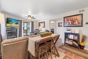 Un salon comprenant un canapé, une table à manger avec des tabourets, une cheminée, un ventilateur de plafond et une bibliothèque.