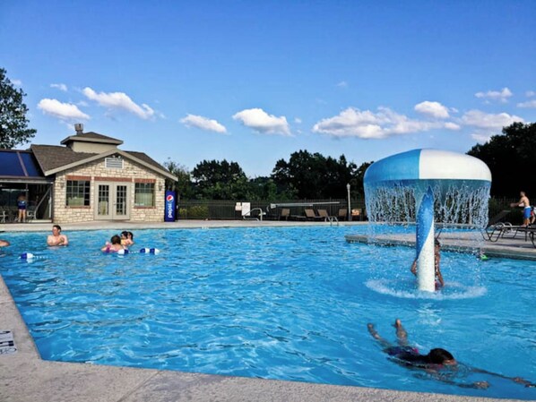 Une piscine agrémentée d’une fontaine, un bâtiment doté d’un toit en pente et un ciel d’un bleu limpide.