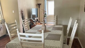 Een eethoek met een tafel voor vier personen, omringd door witte stoelen en een tafelkleed met bloemen.