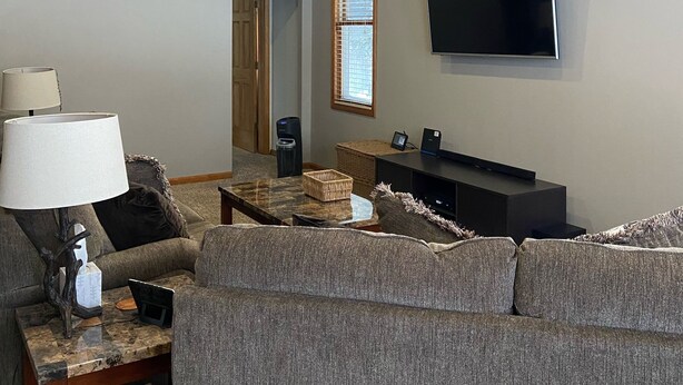 A living room with a ceiling fan, a flat-screen TV mounted on the wall, a sofa, a coffee table, and a lamp.
