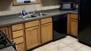 A kitchen with wooden cabinets, a microwave, a dishwasher, and a window with blinds.