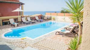 A swimming pool with lounge chairs and umbrellas, surrounded by a stone patio and a view of the sea. - Villa Aris - Holiday & relaxation (Corfu - Kerkyra)